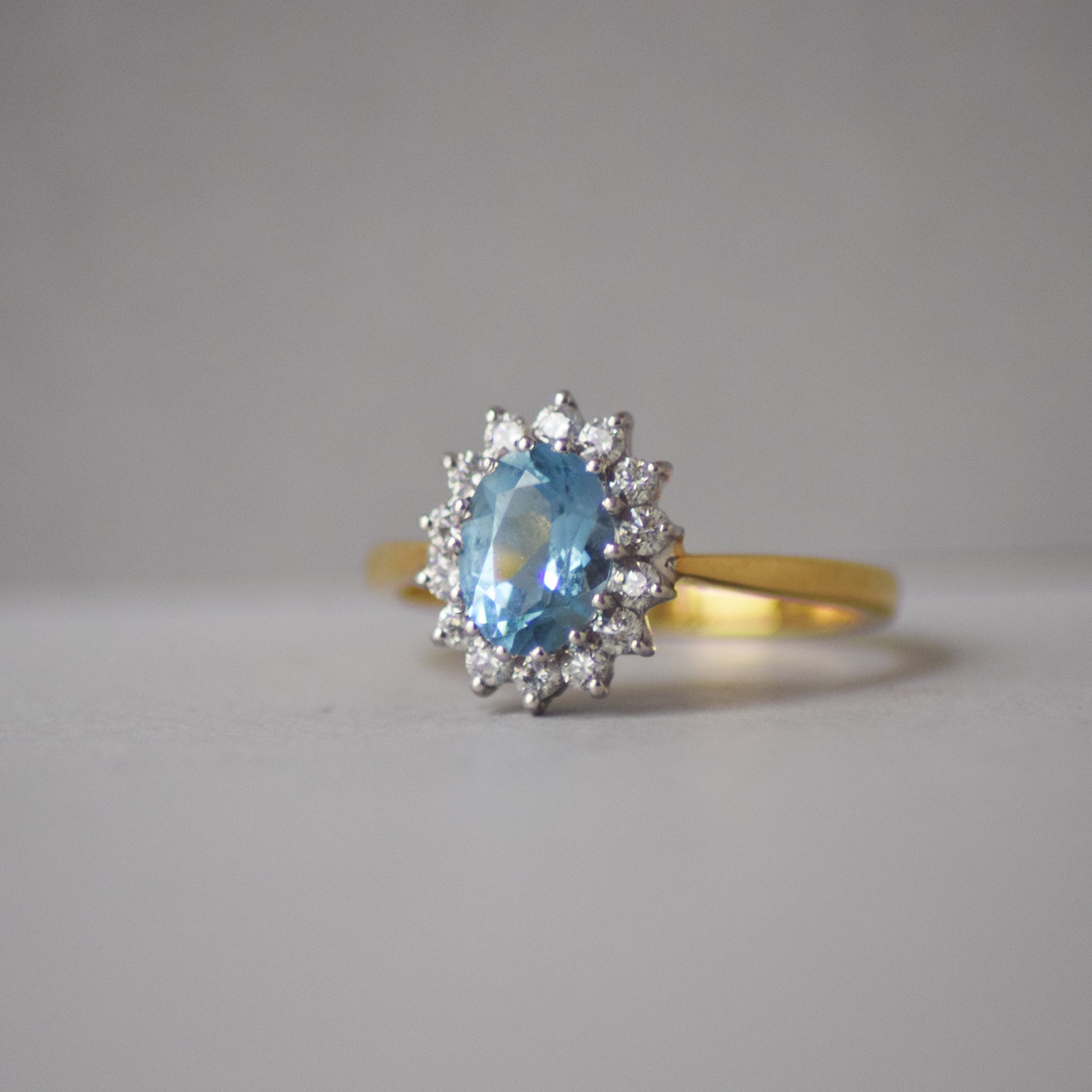 Gold ring with a blue gemstone and diamond accents on a gray background