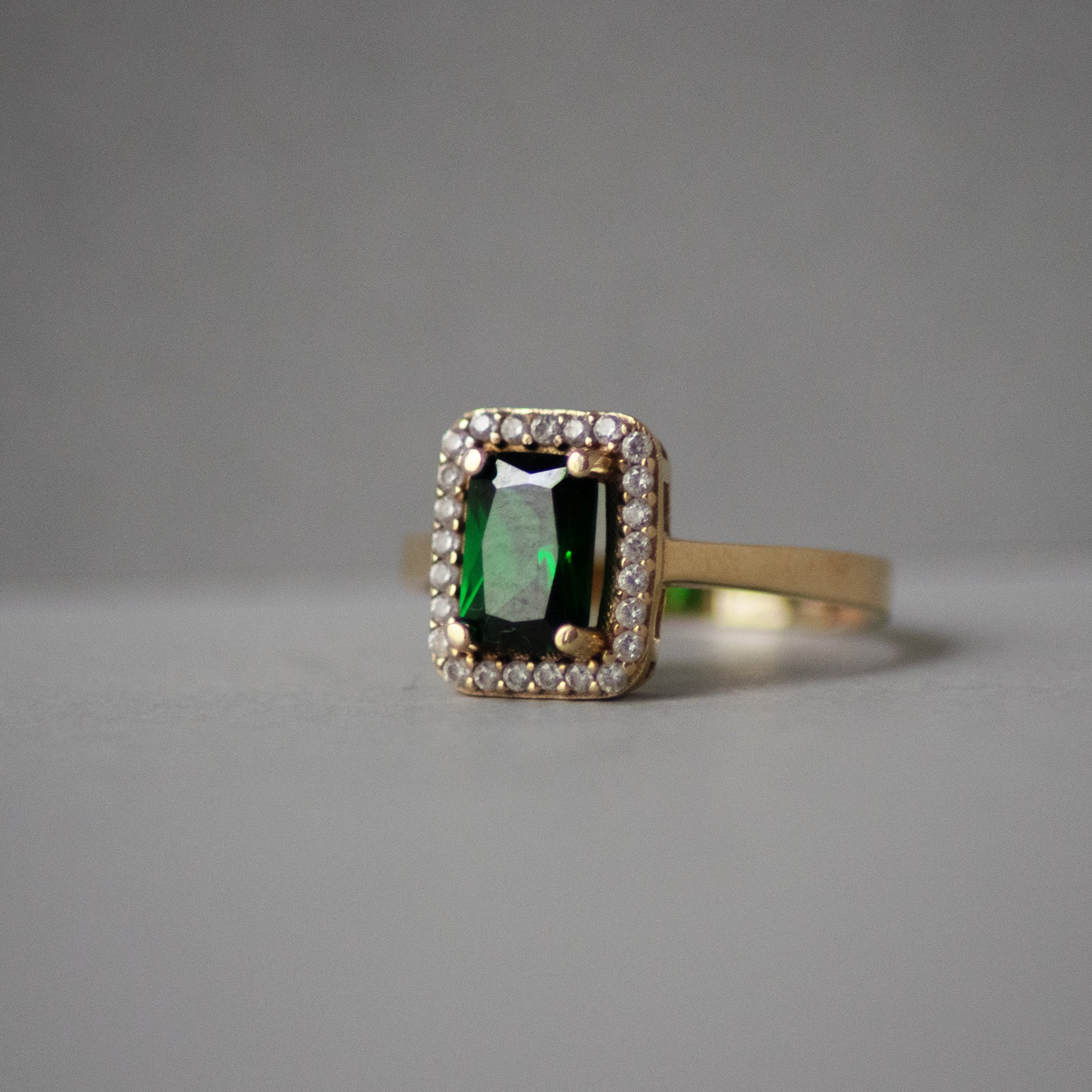 Gold ring with a green gemstone and diamond accents on a gray background