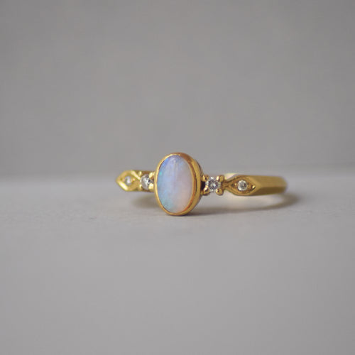 Gold ring with an opal stone and small diamonds on a gray background
