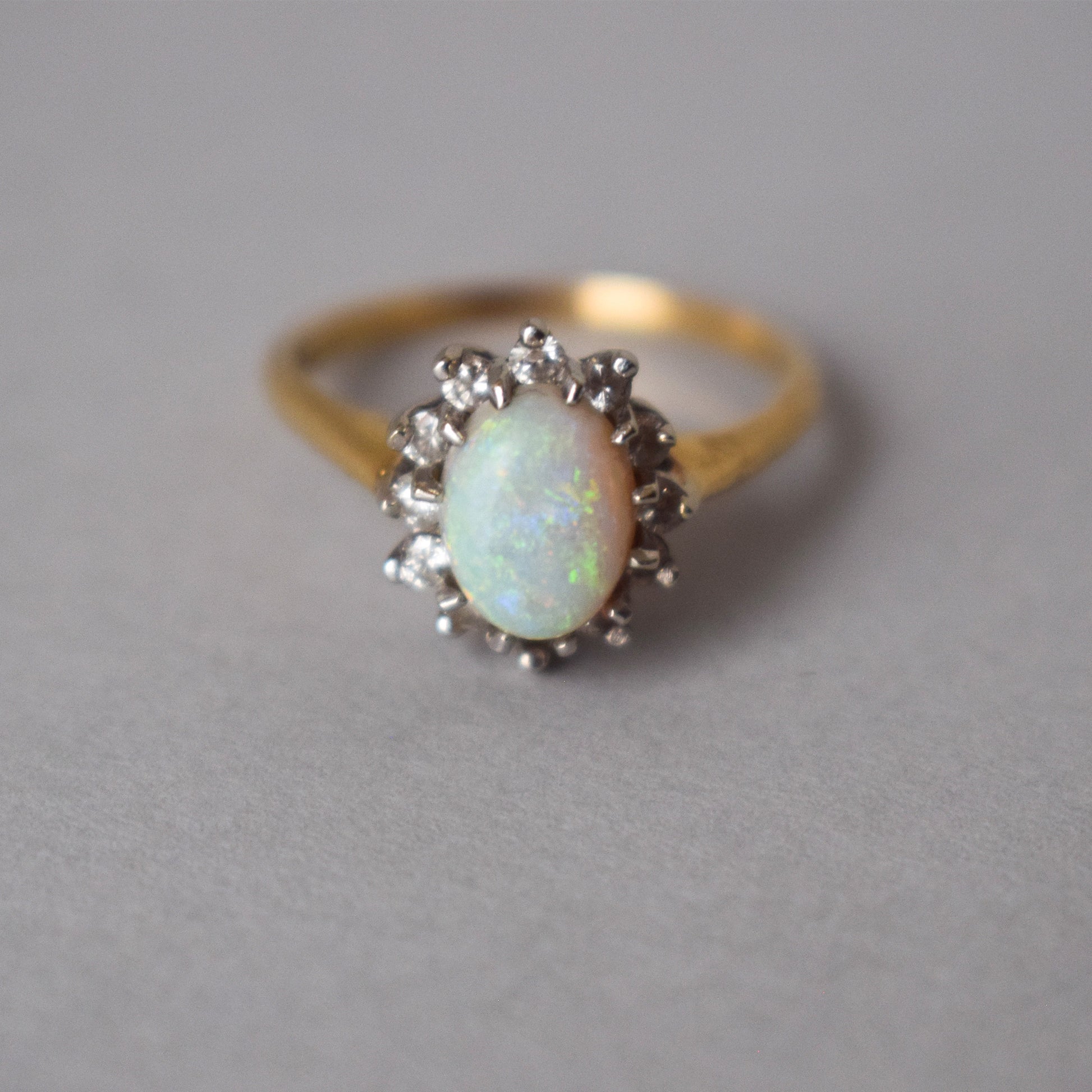 Gold ring with an opal stone and diamond accents on a gray background