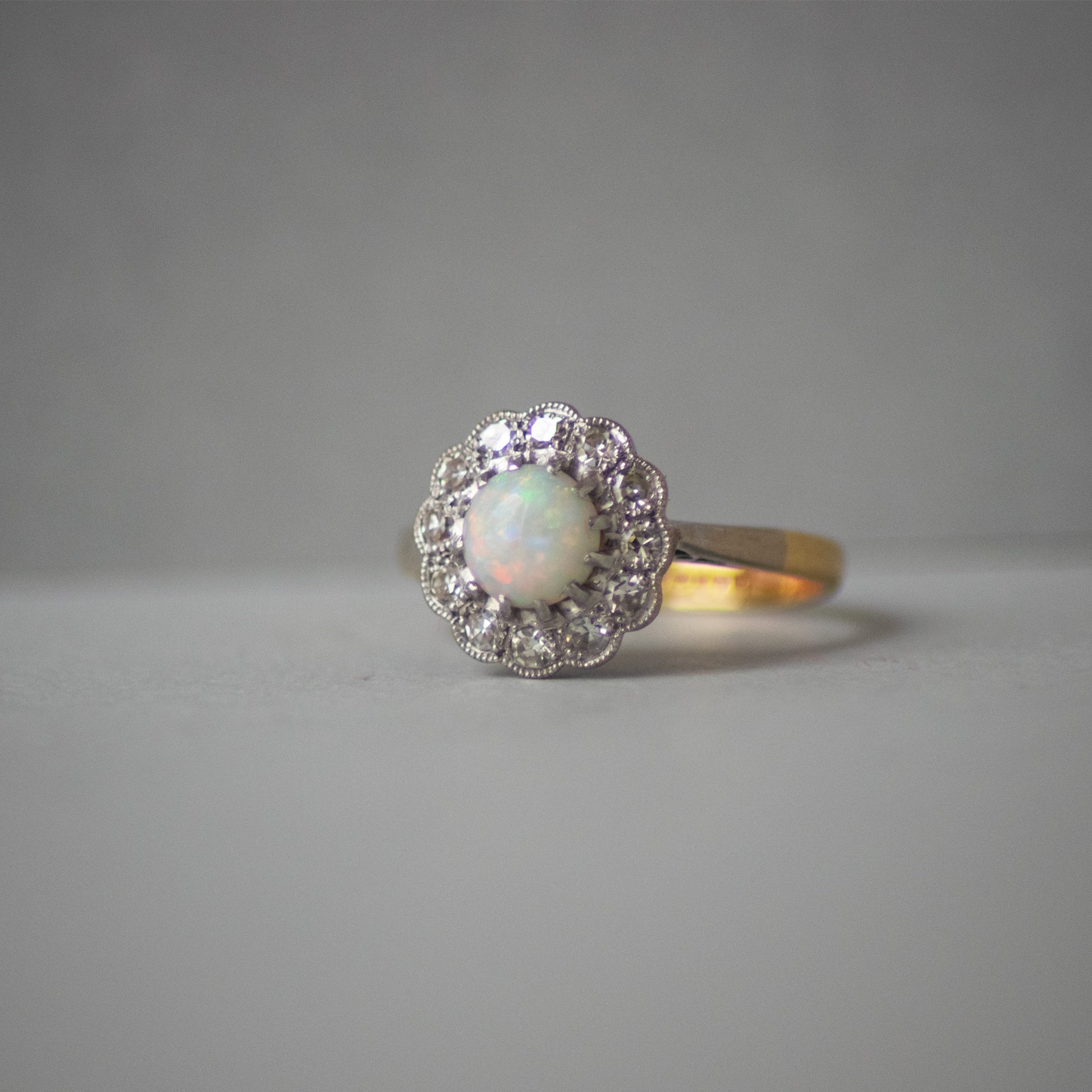 Ring with opal stone and diamond halo on a gray background