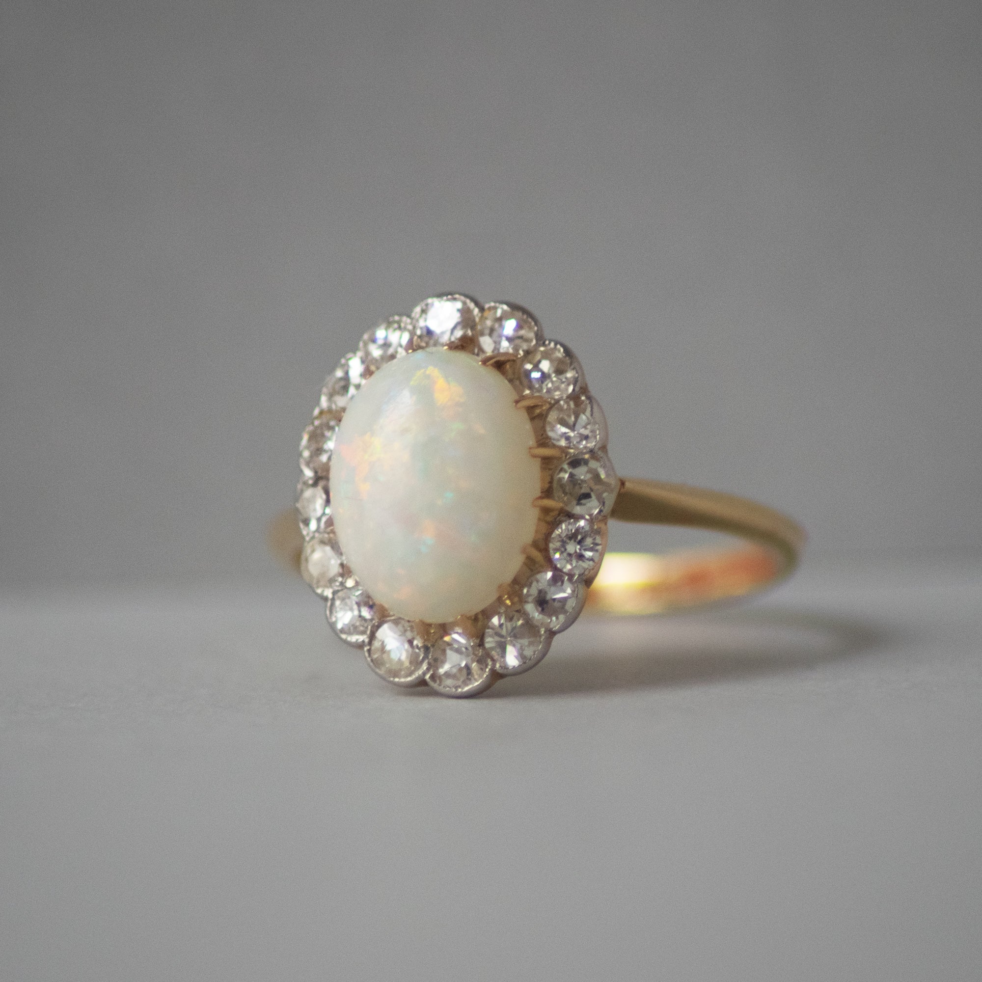 Gold ring with an opal stone and diamond accents on a gray background