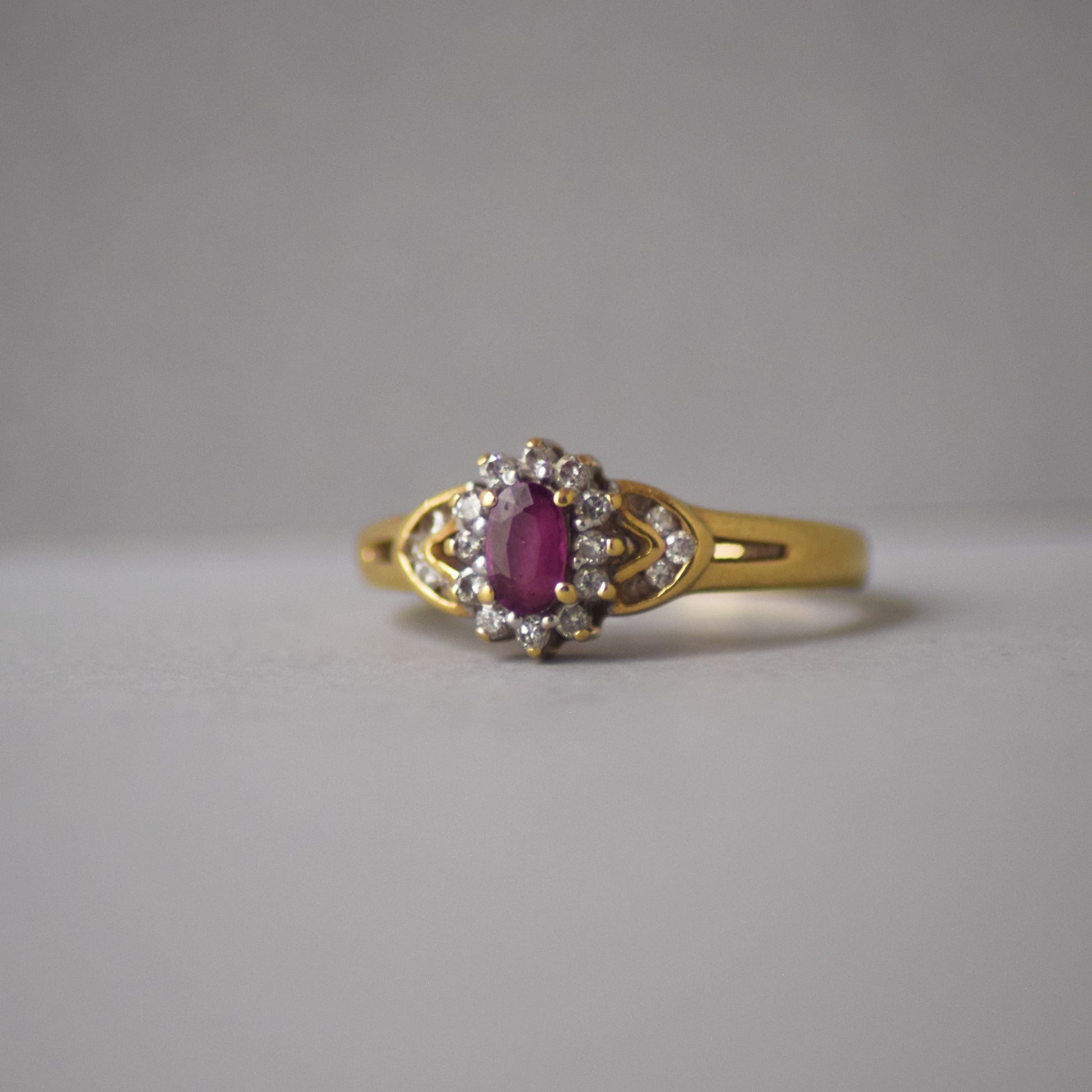 Gold ring with a red gemstone and diamond accents on a gray background