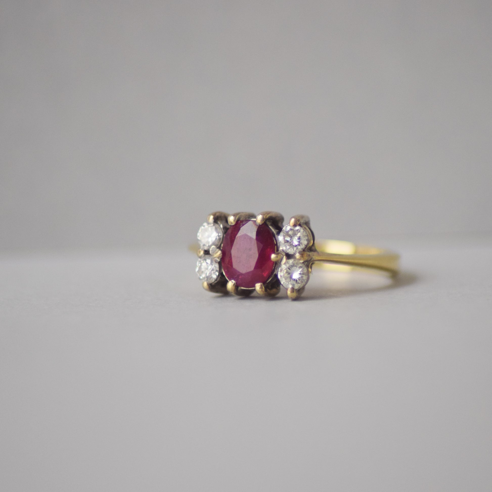 Gold ring with a red gemstone and smaller diamonds on a gray background