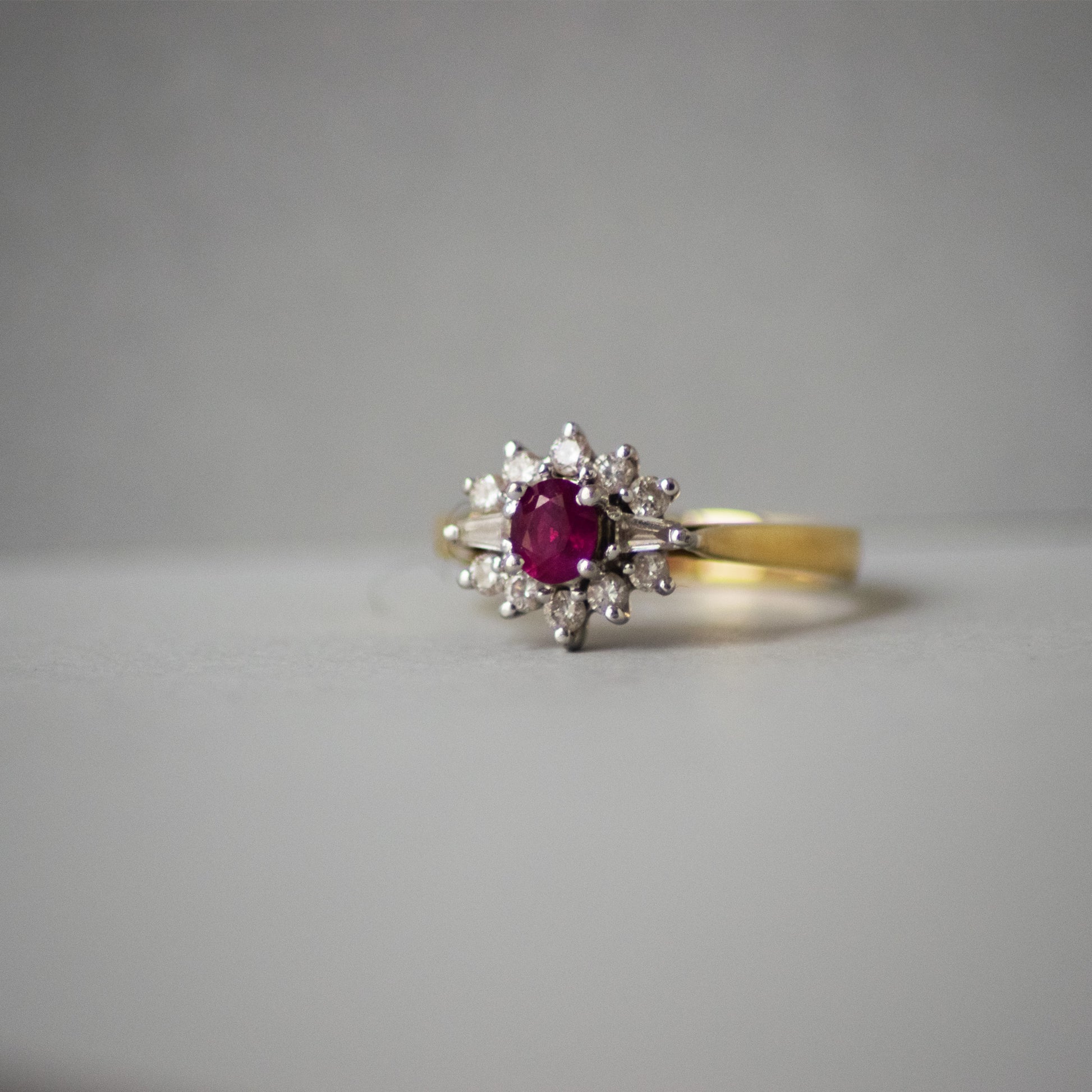 Gold ring with a red ruby gemstone and diamond accents on a gray background