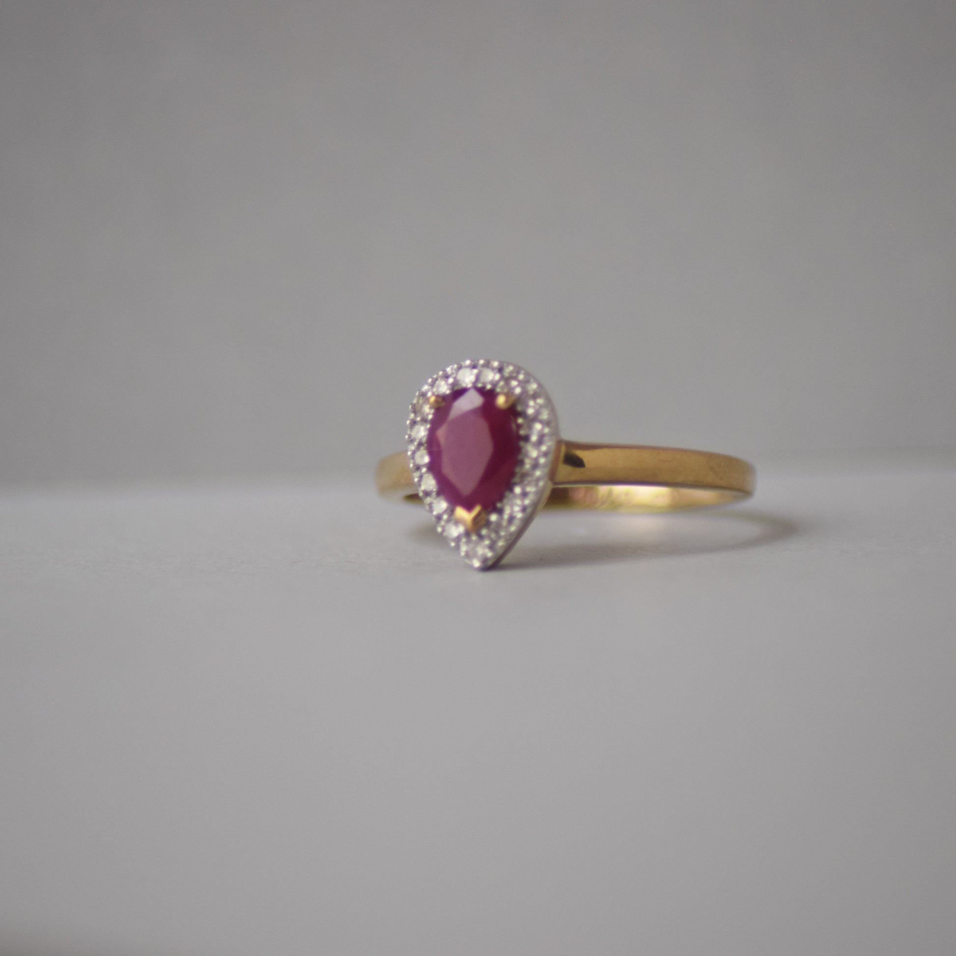 Gold ring with a red gemstone and diamond-studded halo on a gray background