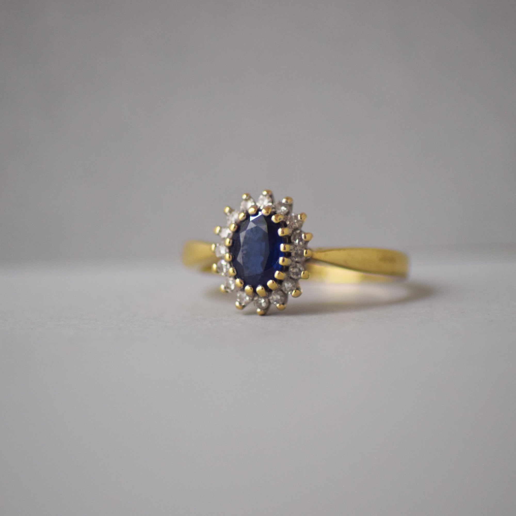Gold ring with a blue sapphire and smaller diamonds on a gray background