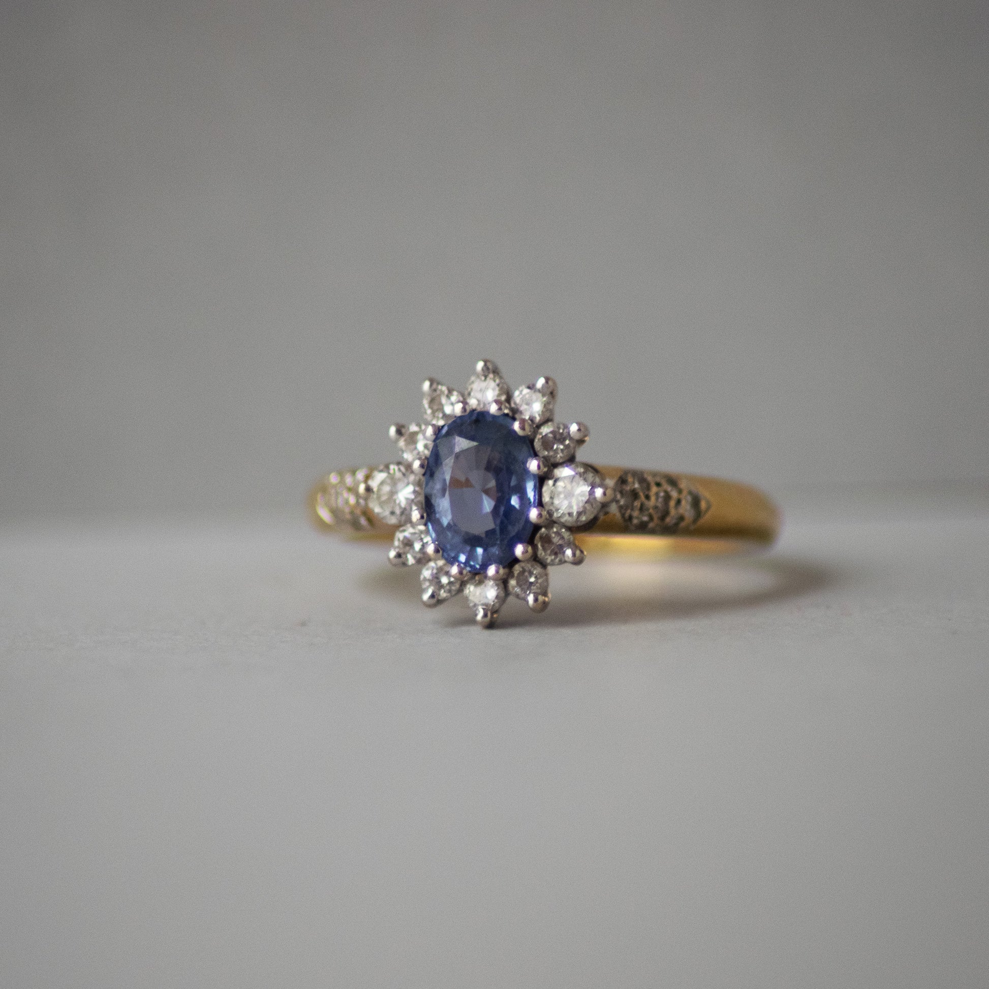 Gold ring with a blue gemstone and diamond accents on a gray background